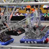 Two robots hang from a bar during a match